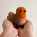 Hand holding a small felted bird toy against a plain background