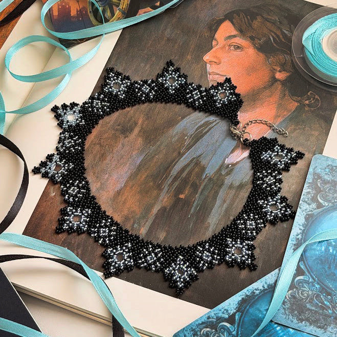 A square beaded mirror with a black and white floral lace border, displayed on top of a vintage-style portrait print. The scene is styled with light blue ribbons, a spool of light blue ribbon, and blue patterned paper on a light-colored surface.